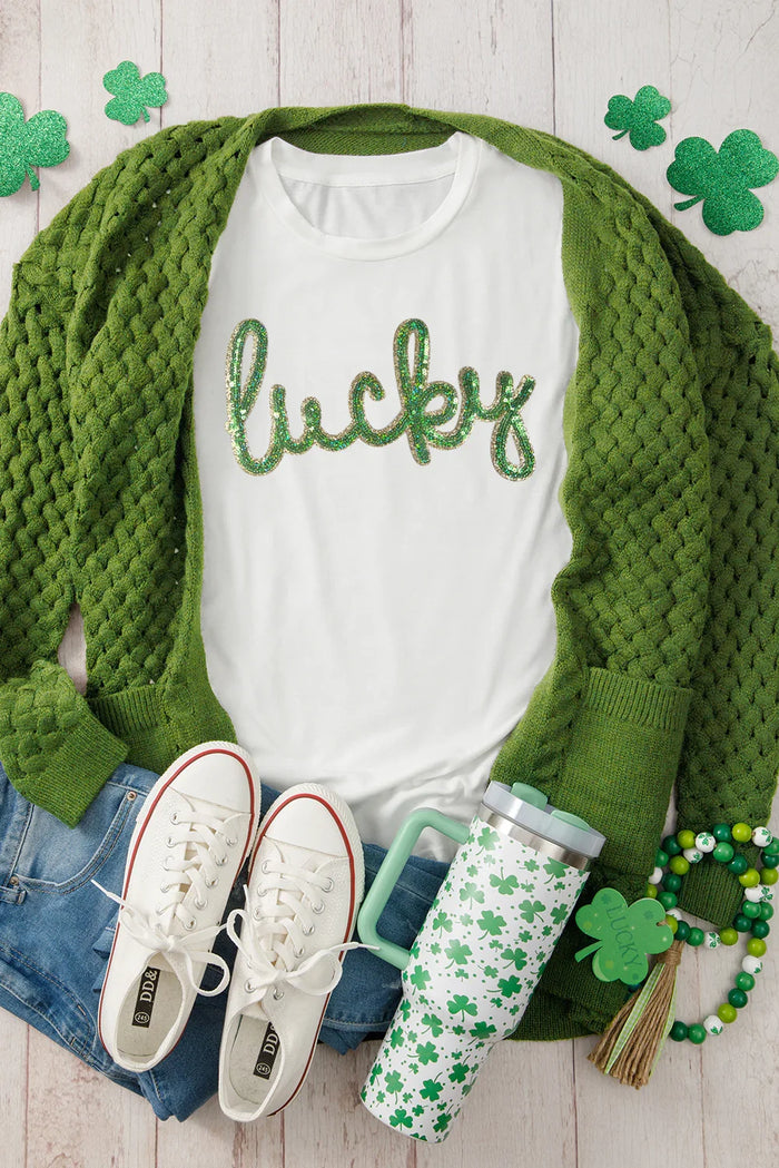 White shirt with 'lucky' text, green cardigan, white sneakers, and green accessories on a wooden surface.