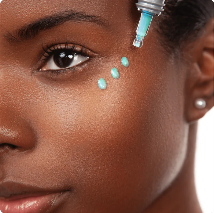 Close-up of a woman's face with dropper applying opti crystal serum to her undereyes.