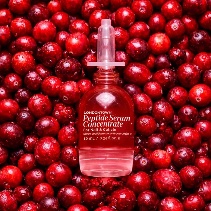 A bottle of LONDONTOWN Peptide Serum Concentrate rests on a bed of fresh cranberries.