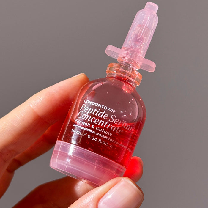 A hand holds a small bottle of LONDONTOWN Peptide Serum Concentrate, filled with pink liquid—ideal for nail repair and cuticle care.