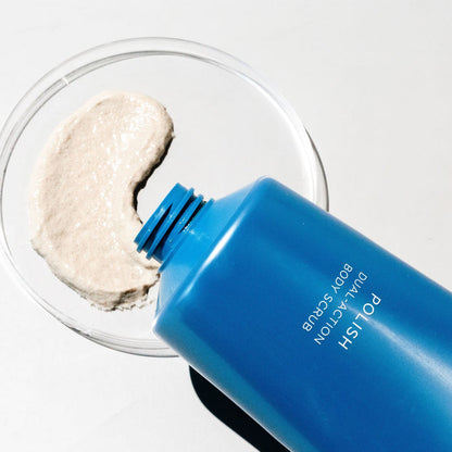 Blue Polish Dual-Action Body Scrub tube with beige exfoliant on a clear glass dish.