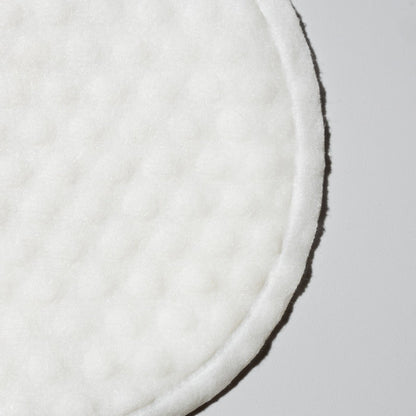 Close-up of a round white textured exfoliating pad against a pale background