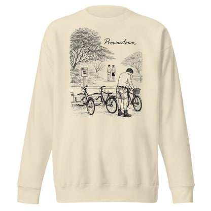 A cream-colored crewneck sweatshirt featuring a black line art graphic of a person with bicycles in a park, with the word 'Provincetown' printed above the illustration.
