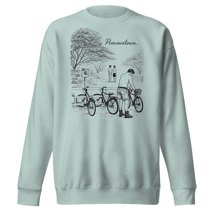 A sage green crewneck sweatshirt featuring a black line art graphic of a cyclist in a park with the word 'Provincial.' printed above, displayed on a solid white background.