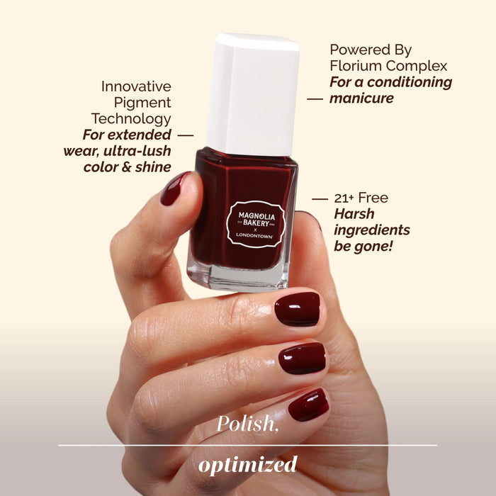 A hand displays manicured nails while holding a bottle of LONDONTOWN’s Red Velvet—a deep burgundy polish featuring a decadent, innovative pigment, a 21+ free formula, and nourishing conditioning properties.
