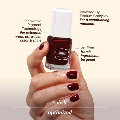 A hand displays manicured nails while holding a bottle of LONDONTOWN’s Red Velvet—a deep burgundy polish featuring a decadent, innovative pigment, a 21+ free formula, and nourishing conditioning properties.