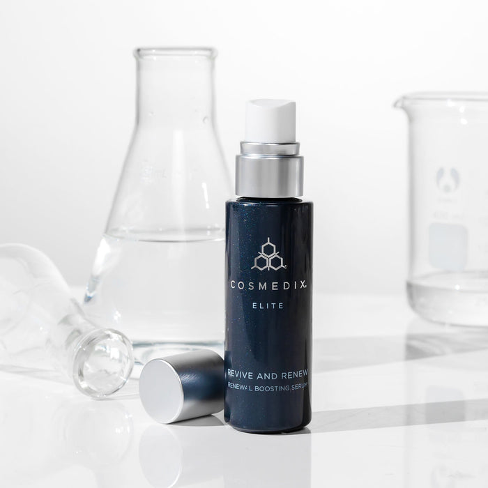 CosMedix Elite Renewal Boosting Serum bottle with dropper cap on a white surface, lab glassware in the background