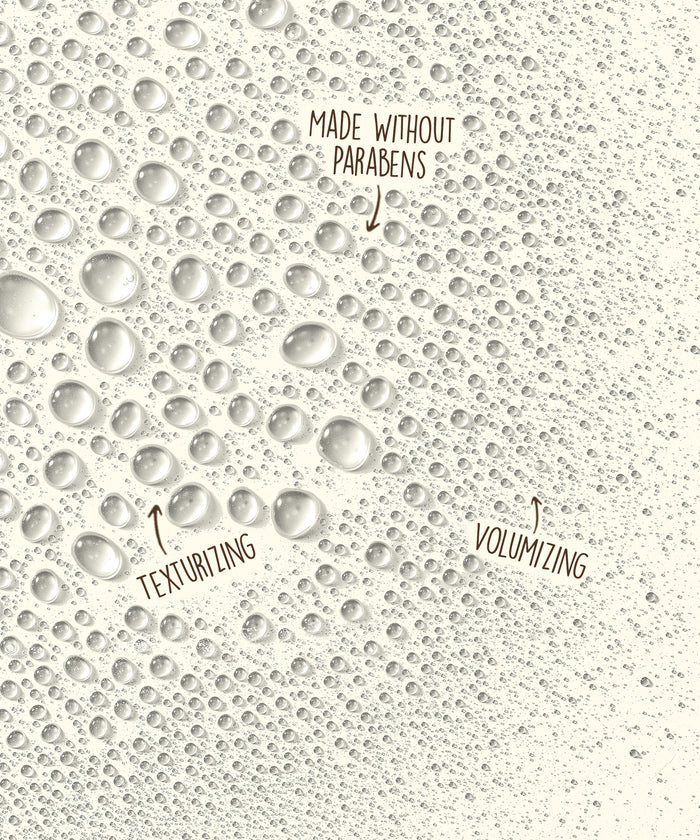 Close-up of clear water droplets on a light surface highlighting Sea Spray by Sun Bum’s volumizing and texturizing effect without parabens.