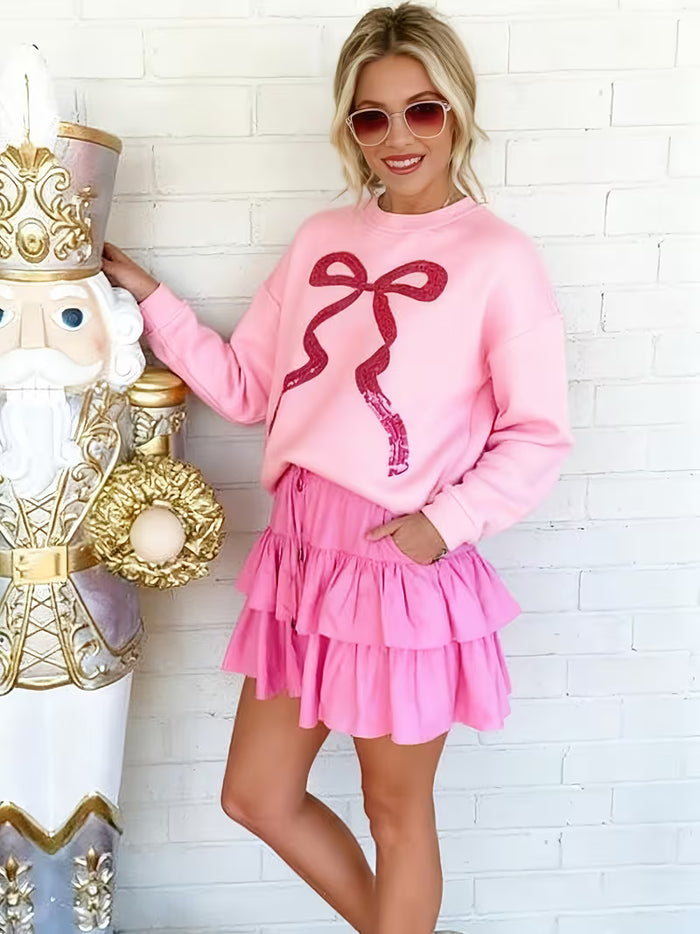 Woman in pink outfit with bow design standing next to a decorative nutcracker against a white brick wall.