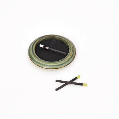 Green ceramic incense tray with black incense pad and two incense sticks