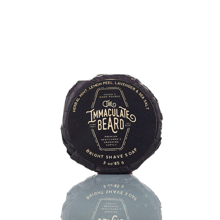 The Immaculate Beard shave soap puck in a round soap dish, showing its creamy, textured surface for a close shave.