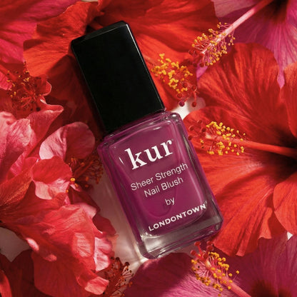 A bottle of LONDONTOWN Sheer Strength Nail Blush - Hibiscus, a nourishing nail hardener, sits among vibrant red hibiscus flowers.