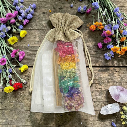 Drawstring bag with sage, selenite, and palo santo on a wooden surface with flowers and crystals around.