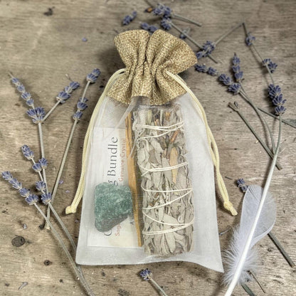 Sage smudge bundle in a drawstring bag with lavender and a feather on a wooden surface