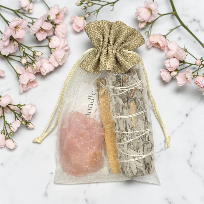 Smudge & Crystal Cleansing Bundle - Rose Quartz on a marble surface with pink flowers.