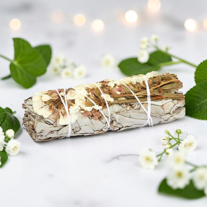 Bundled sage with white twine on a light background with green leaves and flowers.