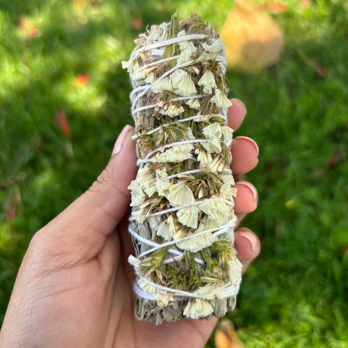 Hand holding a bundle of dried herbs wrapped in twine against a grassy background