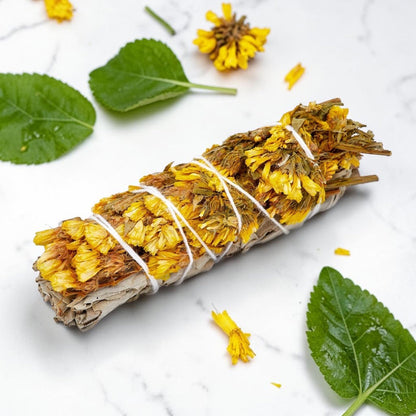 Rolled sage with yellow flowers tied with twine on a white background with leaves and flowers.