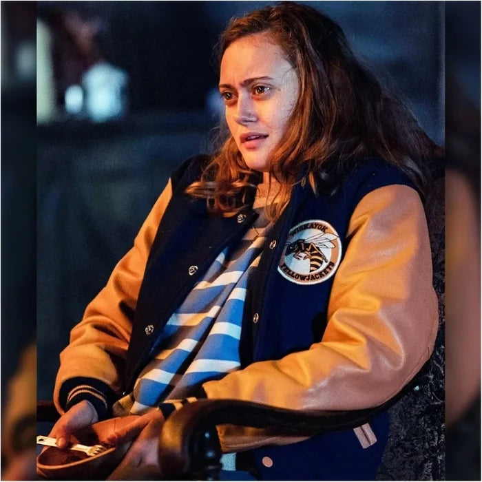 Person wearing a letterman jacket with a logo, sitting indoors.